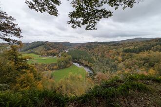 A view along a river in Belgium, with trees covering the slope on one side and fields on the other